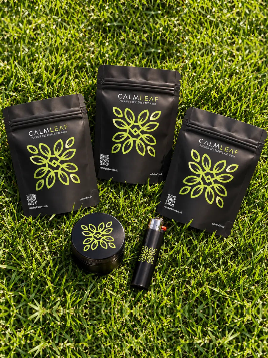 Calm Leaf pouches with a branded grinder and lighter on grass